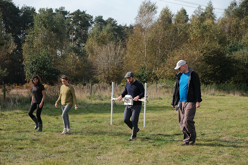 four people walking in field with magnetometer